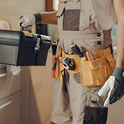 Close up of repairman in uniform standing on home kitchen and holding his tool bag